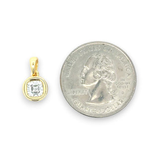 A small gold pendant with a clear square-cut gemstone is shown next to a U.S. quarter for scale on a plain white background.