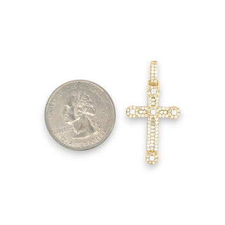 A gold cross pendant paved with small clear stones, shown next to a US quarter for scale on a plain white background.