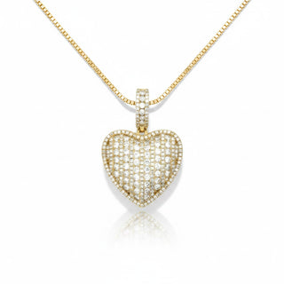 A gold heart-shaped pendant necklace paved with small clear stones, suspended from a gold box chain on a white background with a soft reflection below.