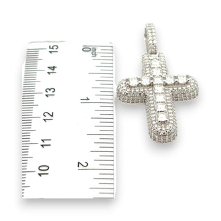 A silver cross pendant encrusted with clear stones, shown next to a white ruler for scale on a white background.