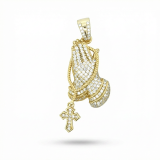 A gold praying hands pendant adorned with pave-set clear stones, featuring a dangling cross charm, shown against a plain white background.