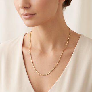 Superior Silver 18-inch 10K yellow gold box link chain worn around a woman's neck, featuring a delicate square weave.