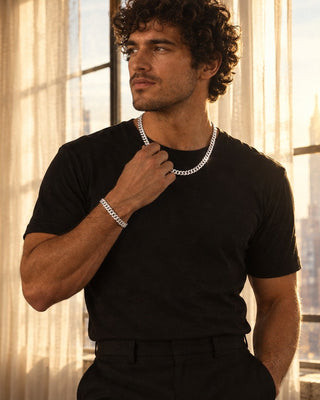 Man in a black tee wearing a 5.7mm sterling silver Miami Cuban chain and Cuban bracelet by a sunlit loft window