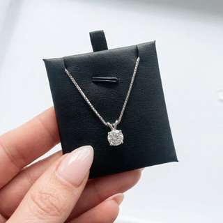 Silver necklace with a round pendant on a black jewelry box held by a hand.
