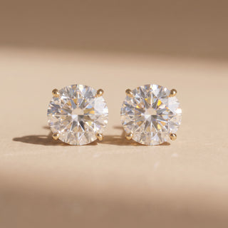 Superior Silver Portuguese cut moissanite stud earrings in gold vermeil with a four-prong setting on a neutral surface.